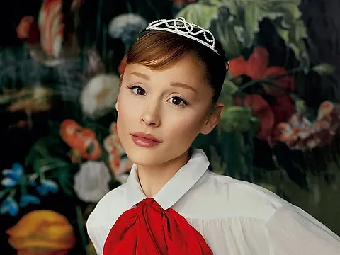 Portrait of a woman in a tiara and a white blouse with a red bow, in front of a painted floral backdrop